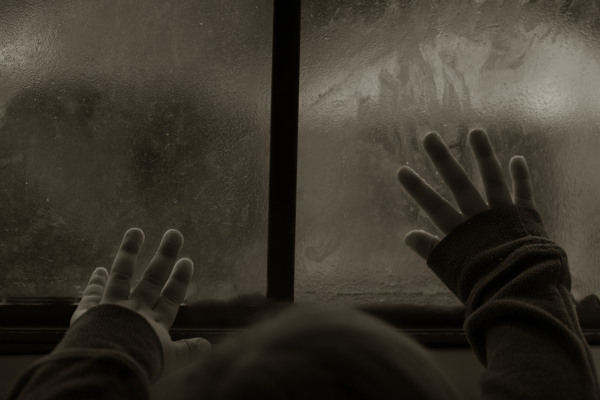 Child hands pressed against textured window in shadow